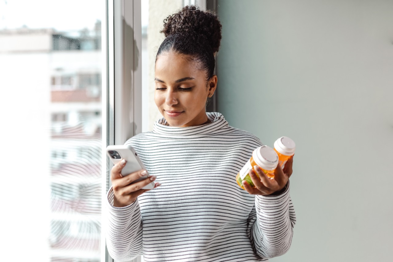 Vrouw bij raam zoekt online informatie over medicijnen in haar hand