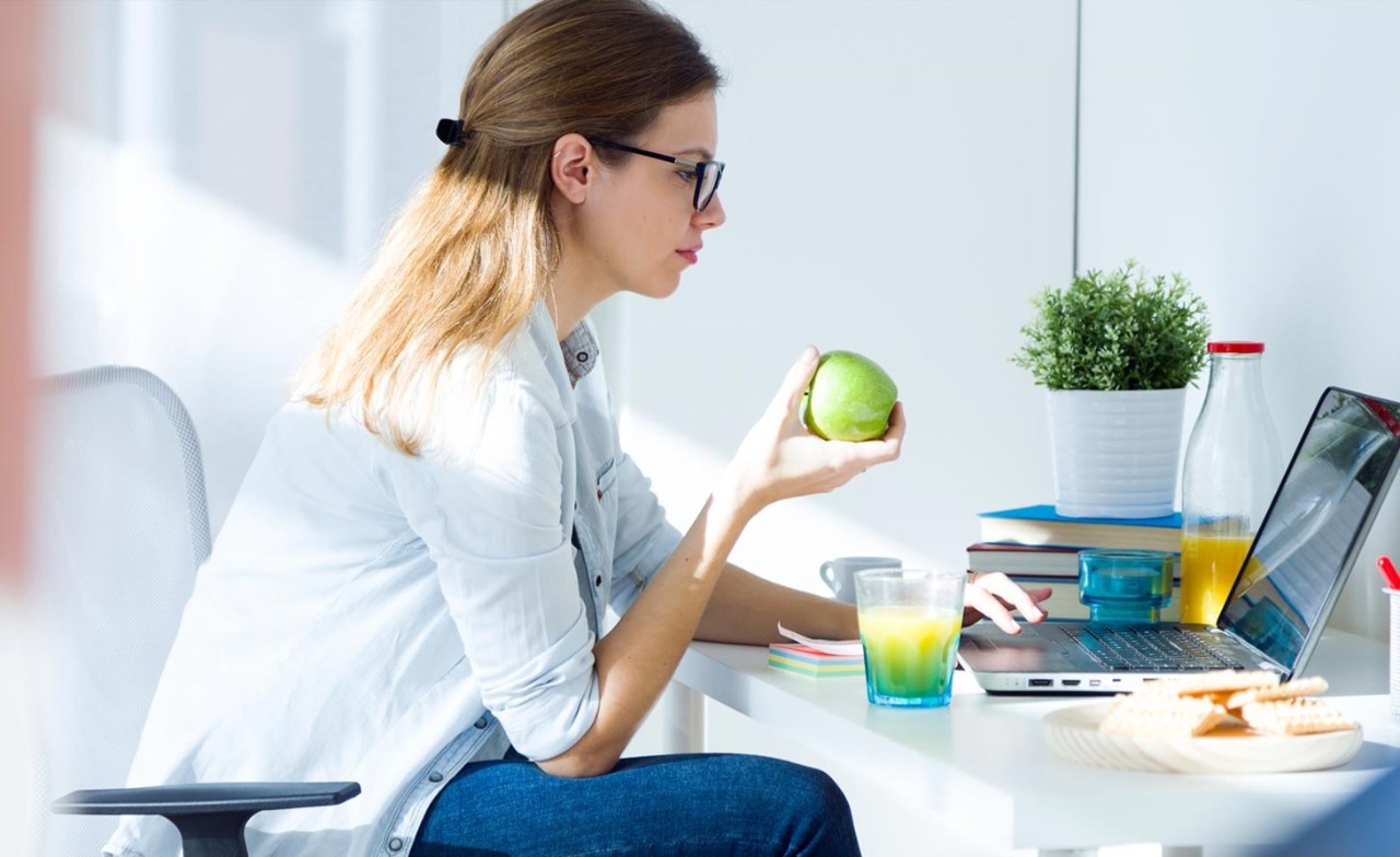 Vrouw eet appel achter laptop