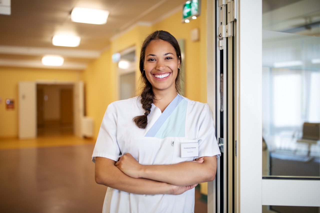 Portrait of confident female nurse at doorway. Smiling nurse standing with arms crossed at hospital.