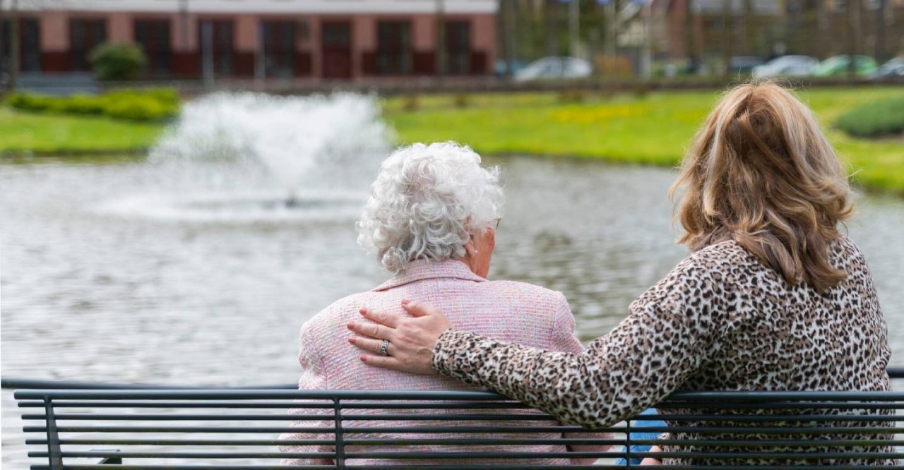 Oudere met begeleider op bankje buiten