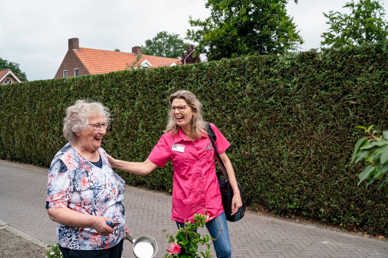 Verpleegkundige in roze met bejaarde vrouw buiten